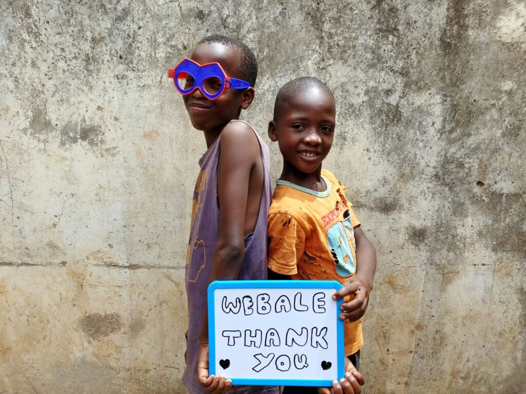 children holding up a whiteboard. text reads 'webale. thank you'