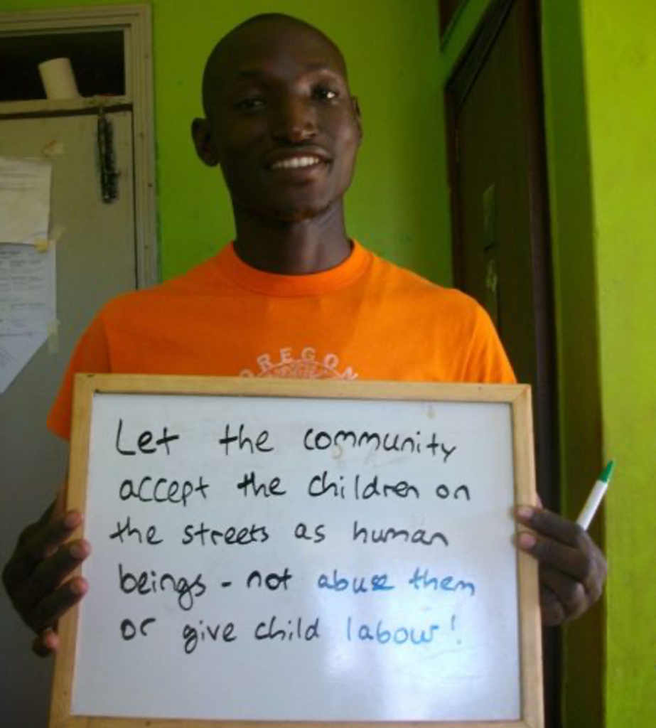 young man holds up a sign reading 'let the community accept the children on the streets as human beings - not abuse them or give child labour