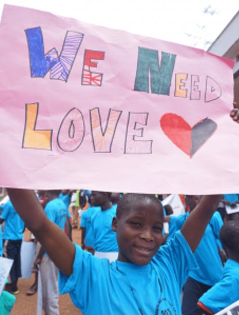 child holds up a sign saying 'we need love'