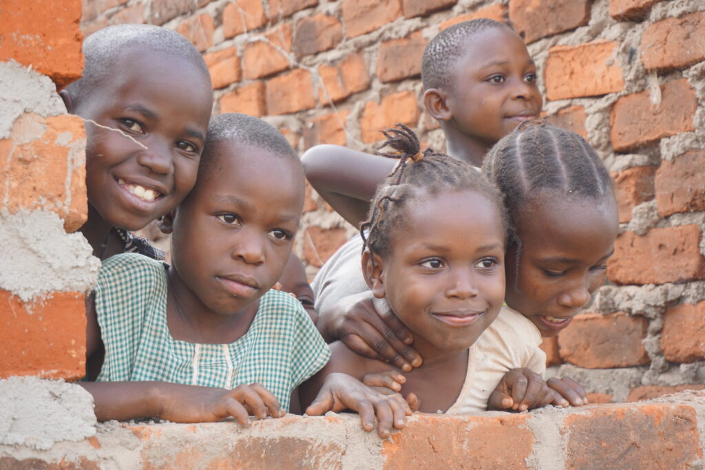 A group of 5 children are pictured smiling over a brick wall
