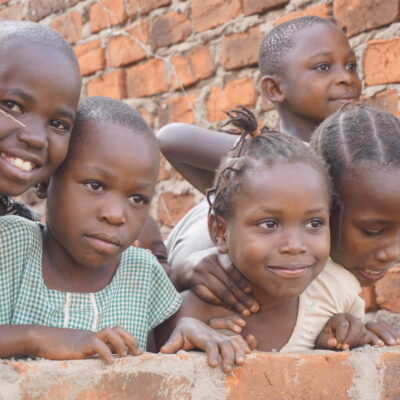 A group of 5 children are pictured smiling over a brick wall
