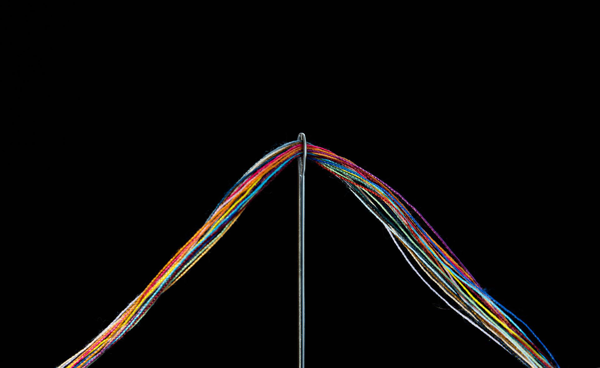 Stock image of multicoloured thread fitting through the eye of a needle
