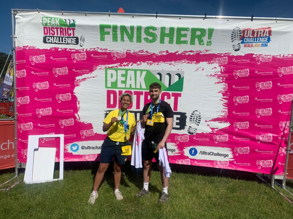 Hafizah and Archie at the finish line of the Peak District challenge holding medals.