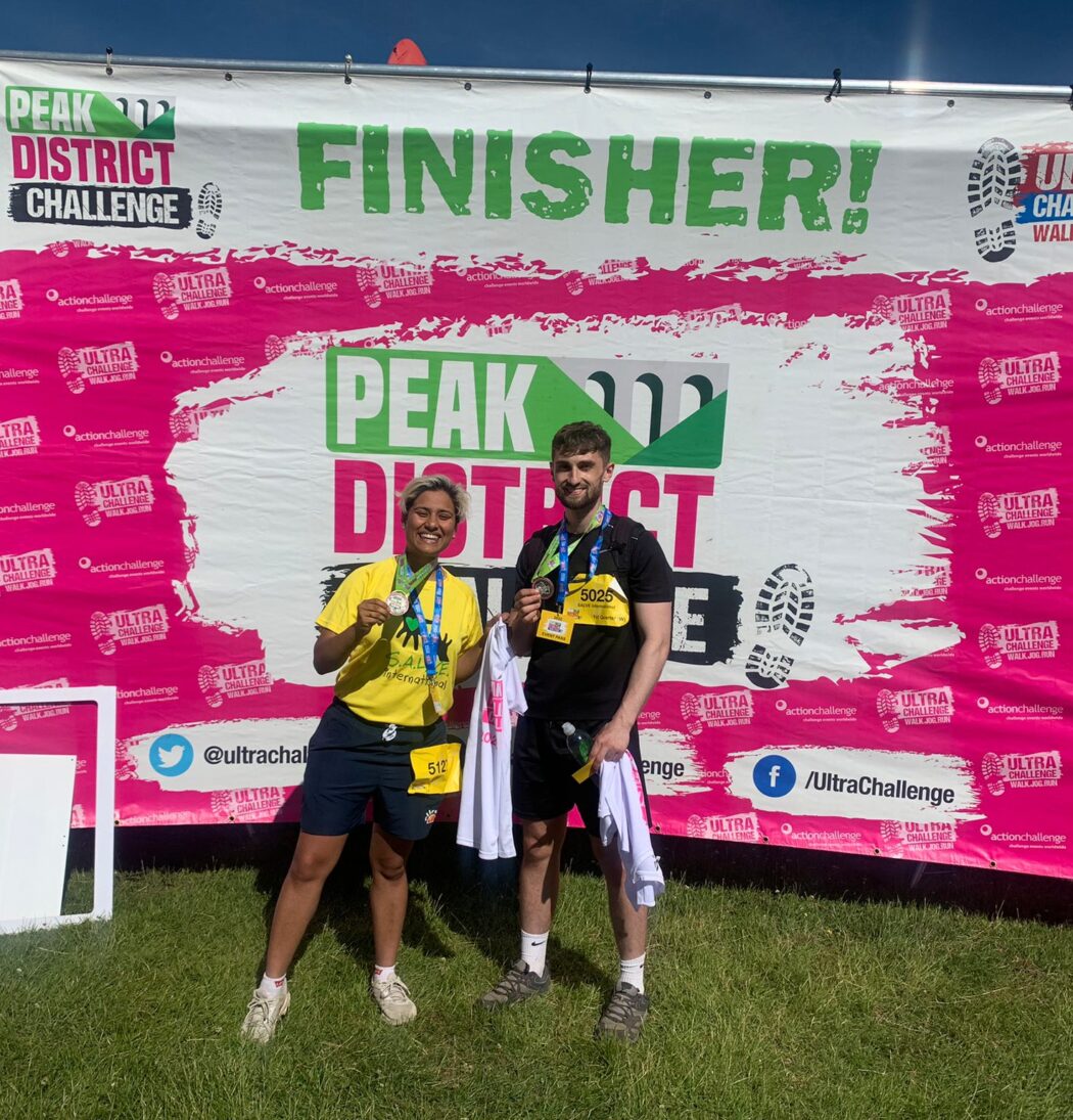 Hafizah and Archie at the finish line of the Peak District challenge holding medals.
