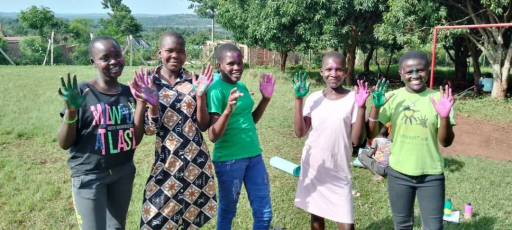 a group of girls, standing outside, smiling and looking at the camera. They have paint on their hands and have been doing art work.