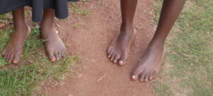 A close up of two pairs of children's feet. Neither have shoes on and they are standing on a dusty path