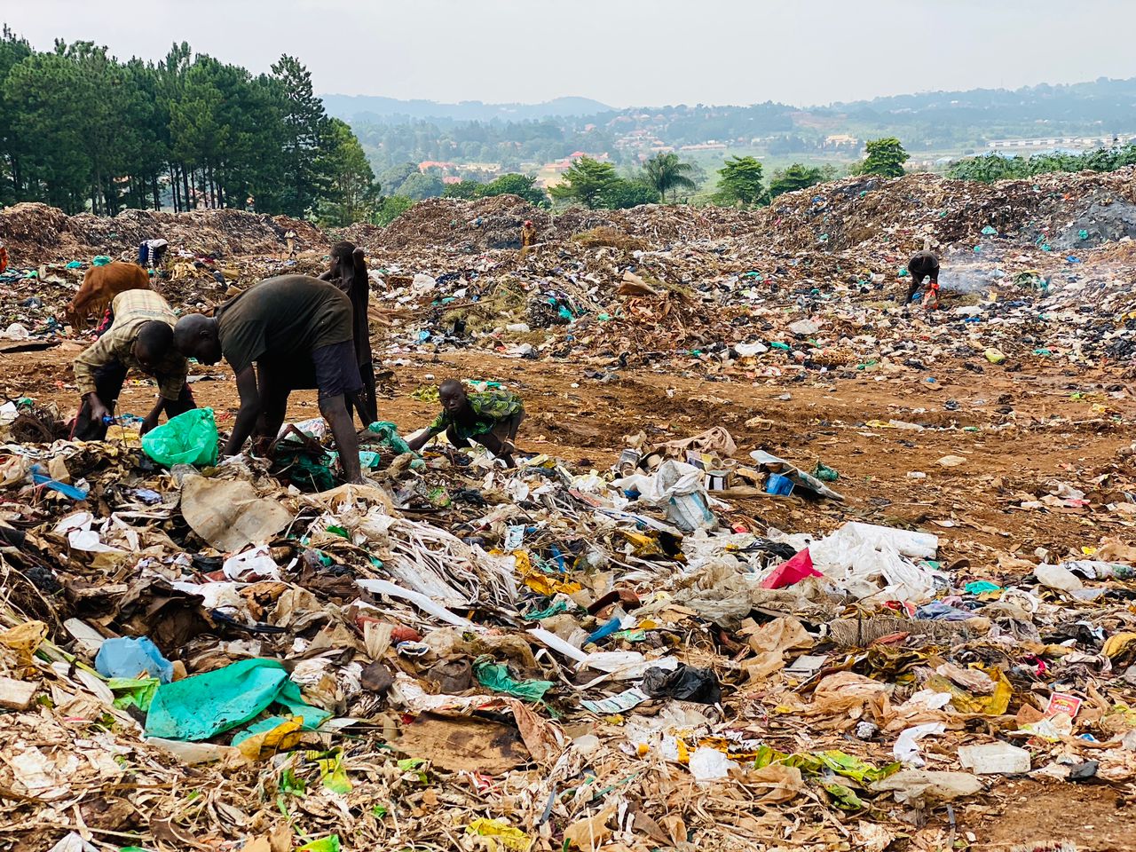 A group of street connected children are looking through a large heap of rubbish for plastic bottles.