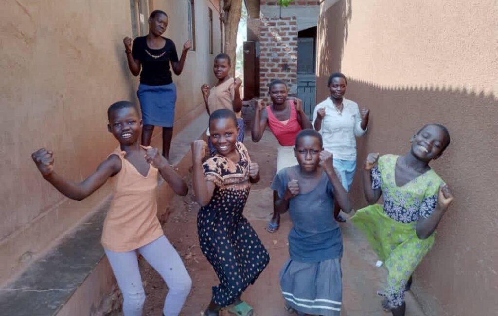 A group of girls at the SALVE drop in centre, posing for the camera. The girls are mimicking strong poses showing their muscles and smiling in a jovial way.