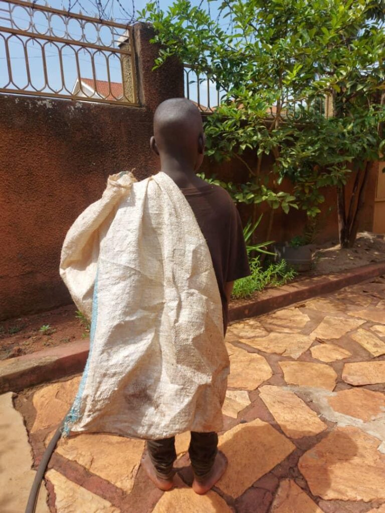 a young boy facing away from the camera, carrying a large empty sack