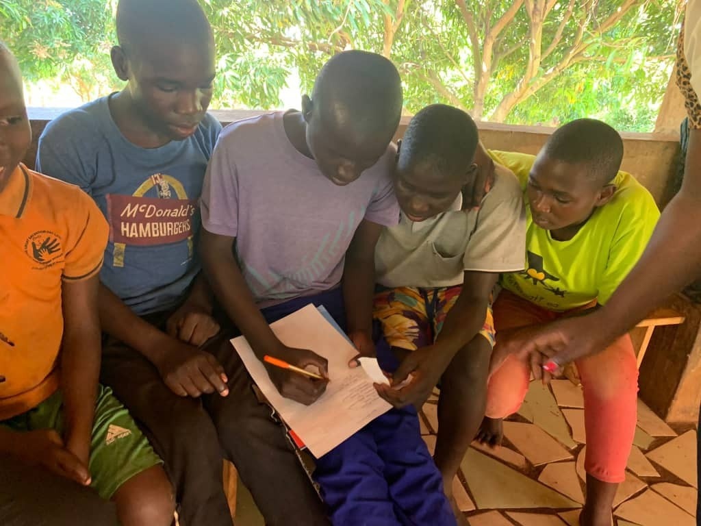 Four children at the SALVE residential site, with one child holding a pen and paper ready to write. All of the children are focusing on the page.