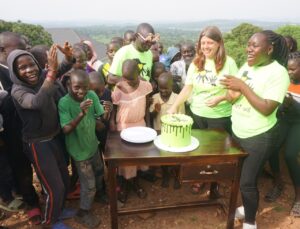 Nicola, CEO of SALVE International, is cutting a birthday cake. Surrounding her are cheering and clapping staff and children.