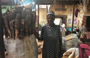A woman is standing beside her market stall, smiling at the camera.
