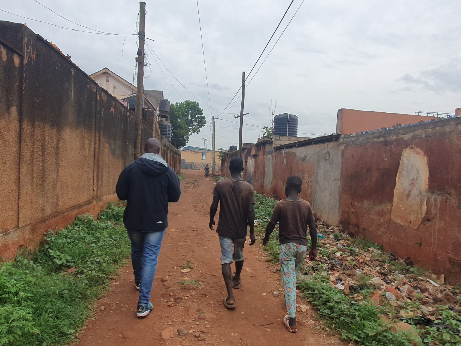 A SALVE staff member and two children are walking down a dusty road between houses