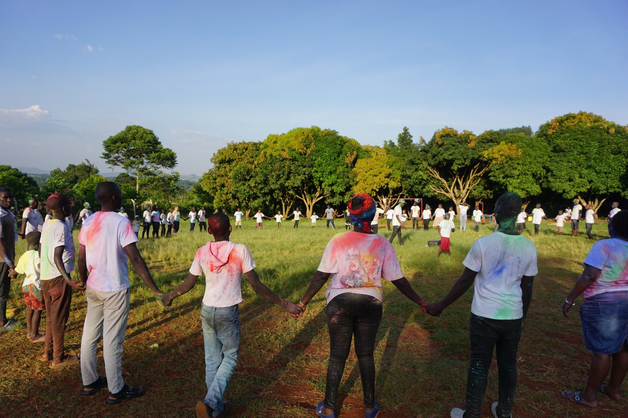 A landscape shot of children and SALVE staff members holding hands in a large circle