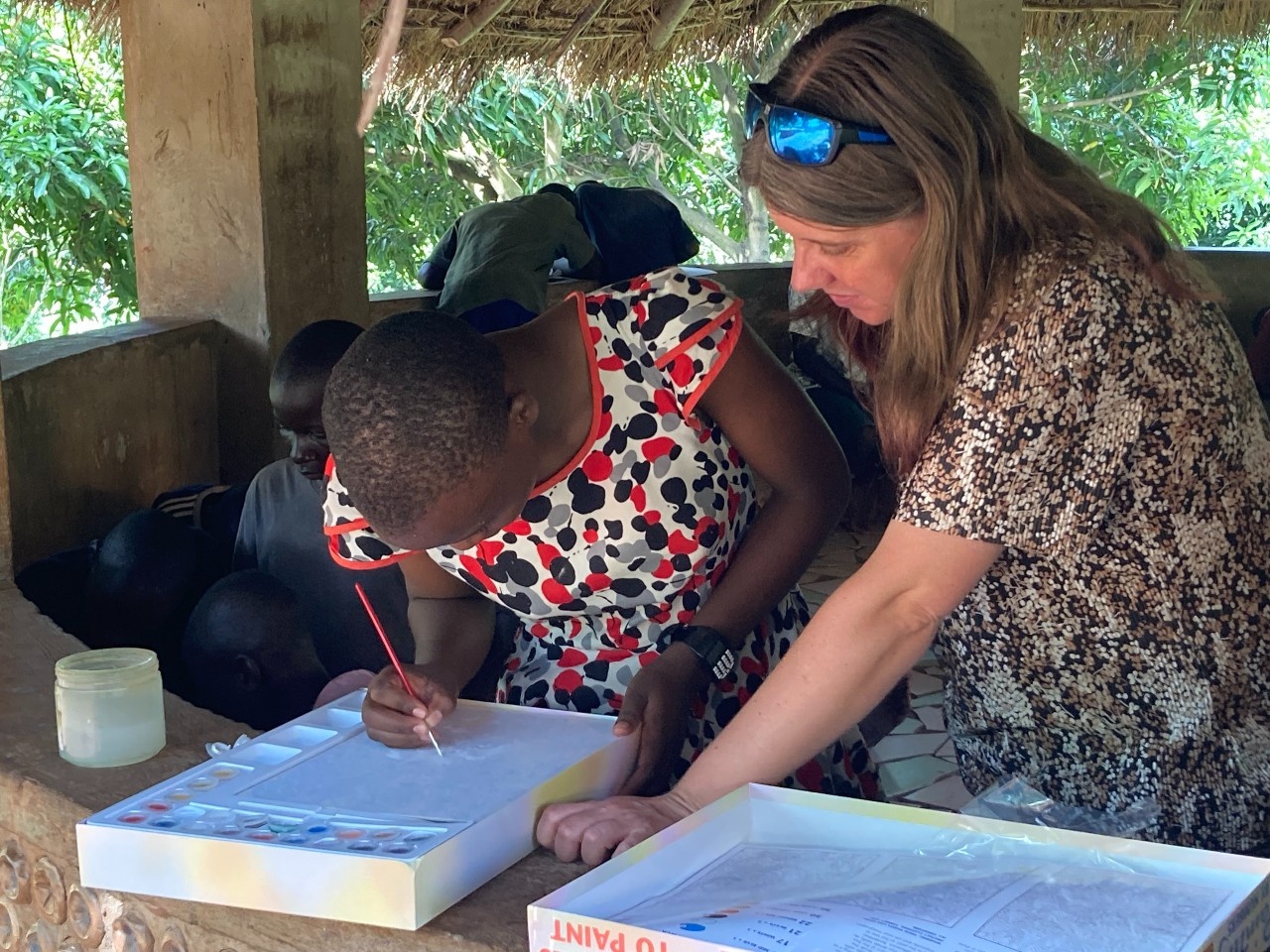 Nicola, CEO of SALVE, is looking at a girl's artwork while she is doing a painting. The girl is concentrating on her work.