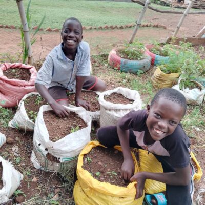 two boys smiling and looking at the camera while sack gardening