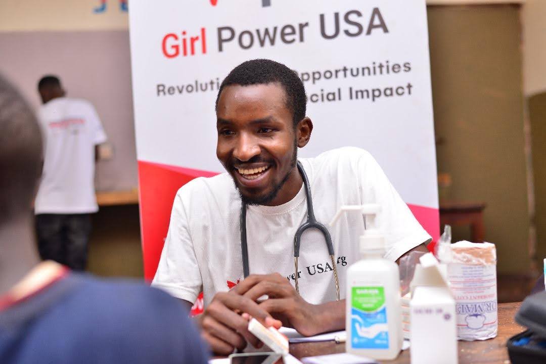 A male healthcare working smiling, sat down in front of a Girl Power USA banner