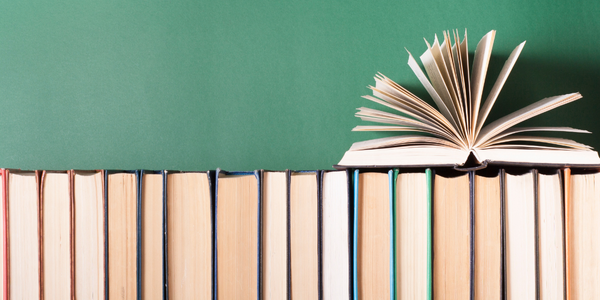 A row of books with one open against a green background.
