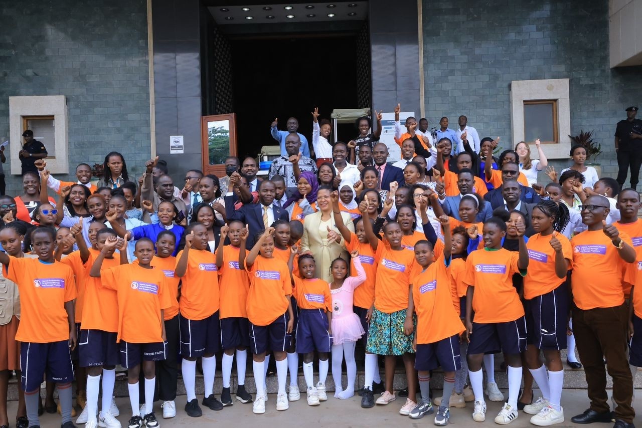 A large group of people smiling for the camera and cheering outside inside the Ugandan Parliament.